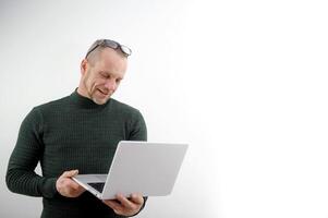 horizontal bandeira do uma lindo sorridente o negócio homem segurando uma computador portátil dentro dele mãos, digitando e navegando a rede, isolado em uma cinzento fundo com uma cópia de espaço foto