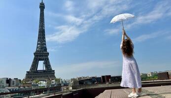 uma lindo jovem menina dentro uma verão vestir carrinhos contra a pano de fundo do a eiffel torre com uma renda guarda-chuva, ela elevado dela mão e Como E se levando fora lá é uma Lugar, colocar para publicidade viagem agência foto