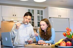 foco em a monitor adolescentes comer Sushi dentro a cozinha assistindo uma filme pais estão não às casa irmão irmã tendo Diversão assistindo uma filme programa encomenda Comida colegas de classe amigos encontro uma amigo foto