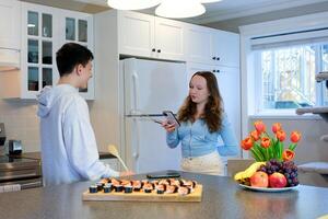 encontro amigos Rapazes menina jogando palavras segurando telefone comunicação Diversão em a mesa Sushi fruta flores primeiro encontro Boa Tempo amor adolescentes ternura ler SMS dizendo uma história foto