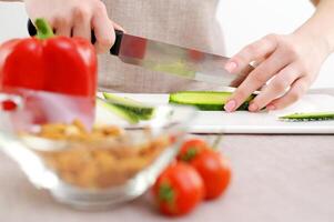 fechar-se lindo fêmea jovem mãos cortar pepino com grande faca vidro prato bege fundo cozinhando delicioso dieta Comida cozinha família lareira salsinha seletivo foco mercearia loja cozinhando Entrega foto