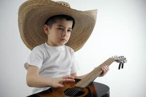 Garoto do pré escola era dentro mãos com guitarra dentro ampla mexicano chapéu senta em branco fundo parece pensativamente inventa melodia escrever música música escola chapéu para crianças musical instrumento loja foto