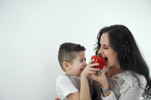 dois amigos mãe morder Sino Pimenta Garoto fazendo careta abraçando espaço para texto Diversão gastos Tempo juntos Piada mercearia loja delicioso legumes vegetariano Comida vestindo avental dentro cozinha mãe e filho foto