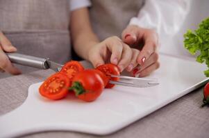 fechar-se do a mãos do a criança e mãe cortar cereja tomates em porcelana borda preparando saudável vegetal salada em corte borda dentro restaurante cozinha Novo magro cardápio, baixo calorias especialidade foto