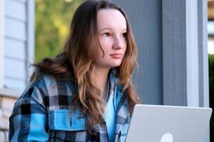 atento mulher assistindo meios de comunicação dentro uma computador portátil dentro uma café fazer compras Adolescência menina dentro azul roupas com fluindo Castanho cabelo senta em a varanda com uma computador portátil e pensa Boa parece lindo pessoas real foto