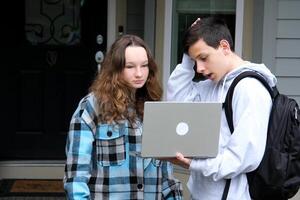 Faz dever de casa juntos peep Garoto e menina sentar Próximo dentro fatos de treino e xadrez menina sorrisos voltas Garoto ajuda encontra erros endireita cabelo desejo curtidas Socorro amigo escola anos colegas de classe adolescentes foto