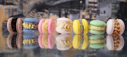 multicolorido macarons mentira em uma vidro mesa com reflexão contra a pano de fundo do uma noite cidade papel de parede Rosa verde amarelo bege azul chocolate macarons delicioso doce sobremesa foto