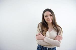 lindo mulher com grandes Castanho cabelo vestindo uma branco banho roupão e sorridente alegremente enquanto posando em cinzento fundo com cópia de espaço foto