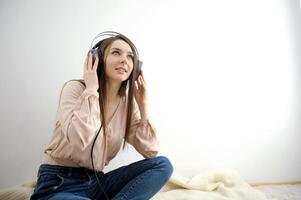 europeu americano mulher Rosa blusa com fones de ouvido atraente alegre mulher ouvindo e desfrutando música dentro fones de ouvido, sorridente, rindo e não olhando dentro Câmera isolado em uma branco fundo foto