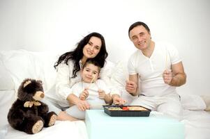 casa Entrega do Sushi feliz alegre família comendo Sushi a partir de descartável talheres com pauzinhos brinquedo Urso de pelúcia Urso perto europeu família feliz comendo dentro cama dia fora gastos Tempo com família idílio foto