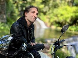 uma homem sentado em uma motocicleta contra a pano de fundo do a natureza do Portugal ele sonhos e parece acima ele tem muito tipo profundo olhos, Sombrio cabelo e uma Preto couro jaqueta, ele é 35-45 anos velho foto