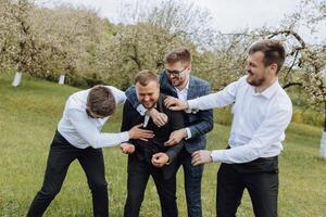 quatro Rapazes vestido dentro ternos e branco camisas, tendo Diversão dentro natureza. a noivo e dele amigos estão a comemorar uma especial evento foto