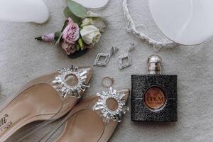 uma par do Alto salto, uma garrafa do perfume, e uma flor estão exibido em uma mesa foto