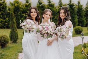 três mulheres dentro branco vestidos estão posando para uma foto com flores dentro seus mãos