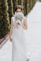 uma mulher dentro uma branco vestir é caminhando baixa uma caminho com uma ramalhete do branco flores foto