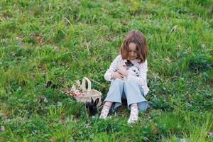 uma jovem menina senta dentro uma campo segurando dois coelhos dentro dela braços foto