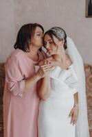 uma mãe abraços dela filha, a noiva, vestindo uma Casamento vestir foto