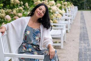 uma sorridente mulher senta sozinho em uma parque banco, incorporando tranquilidade no meio naturezas abraço capturando uma sereno momento do auto aceitação dentro meia-idade jornada. foto