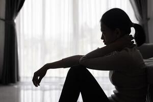 depressivo mulher, silhueta do adolescente menina com depressão sentado sozinho dentro a Sombrio sala. Preto e branco foto. foto