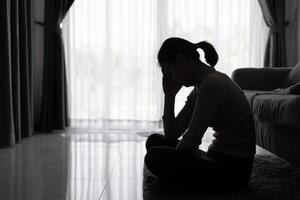 depressivo mulher, silhueta do adolescente menina com depressão sentado sozinho dentro a Sombrio sala. Preto e branco foto. foto