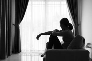 depressivo mulher, silhueta do adolescente menina com depressão sentado sozinho dentro a Sombrio sala. Preto e branco foto. foto