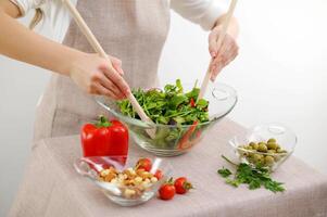 fechar-se do salada amassar com de madeira colheres cereja tomates coquetel pepinos azeitonas bege avental e branco fundo espaço para texto restaurante Comida servindo mesa configuração almoço jantar café da manhã foto