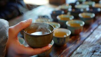 uma alunos mão segurando uma copo do tradicional chá às uma língua evento com diferente chá misturas e seus país do origem listado em a mesa. a vapor Aumentar a partir de a cu foto