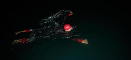 uma determinado profissional triatleta sofre rigoroso noite Tempo Treinamento dentro frio águas, exibindo dedicação e resiliência dentro preparação para a próximos triatlo nadar concorrência foto