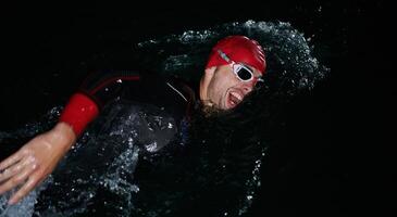 uma determinado profissional triatleta sofre rigoroso noite Tempo Treinamento dentro frio águas, exibindo dedicação e resiliência dentro preparação para a próximos triatlo nadar concorrência foto