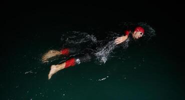 uma determinado profissional triatleta sofre rigoroso noite Tempo Treinamento dentro frio águas, exibindo dedicação e resiliência dentro preparação para a próximos triatlo nadar concorrência foto