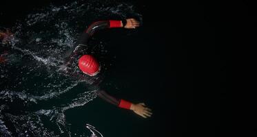 uma determinado profissional triatleta sofre rigoroso noite Tempo Treinamento dentro frio águas, exibindo dedicação e resiliência dentro preparação para a próximos triatlo nadar concorrência foto