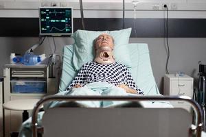Idoso hospitalizado deitado inconsciente na cama do quarto de hospital foto