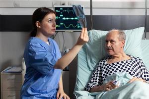 enfermeira médica analisando raio-x de paciente sênior em quarto de hospital foto
