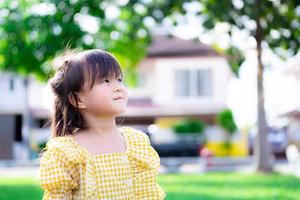 crianças asiáticas são felizes, sorrindo doce e olhando para o céu. fundo é casa borrada e gramado verde. criança de 5 anos.