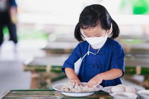 linda garota desempenha papel pequeno fazendeiro. criança usando máscara branca está sentada na cadeira de bambu e cubra os ovos de pato em argila branca. foto