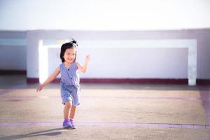 alegre menina asiática tocando e dançando no sol quente com um sorriso brilhante. conceito de bebê feliz. bebê de 2 anos e 9 meses. foto