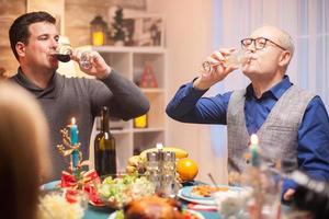 sênior feliz e seu filho bebendo uma taça de vinho juntos foto