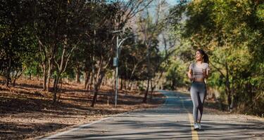 exuberante jovem mulher goza uma manhã correr ao longo uma sereno, arborizada estrada manchado com luz solar. foto