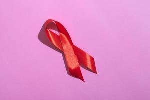 dia internacional da aids. fita vermelha com uma sombra dura em um fundo rosa. ajuda o conceito de conscientização. foto