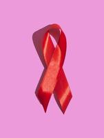 dia internacional da aids. fita vermelha com uma sombra dura em um fundo rosa. ajuda o conceito de conscientização. vertical foto