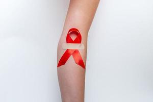 conceito médico para o dia mundial da aids em dezembro. fita vermelha ajuda a consciência agarrada na mão de uma mulher em um fundo branco. fechar-se foto