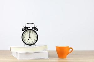 despertador com livros e xícara de café na mesa de madeira e fundo branco foto