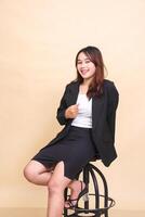 jovem lindo Indonésia executivo menina alegre sorrir sentado em cadeira e pose segurando Jaqueta e cadeira para Câmera, 3 de 4 corpo retrato em amarelo fundo para comercial, tecnologia e o negócio foto