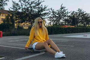 uma jovem Loiras menina dentro uma amarelo suéter passeios em a skate dentro a patim parque foto