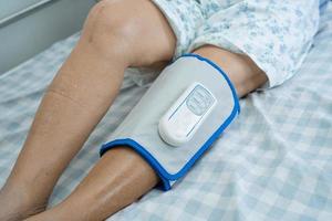 paciente asiático sênior ou idosa com massagem nas pernas de pressão de compressão de ar sem fio na cama em um hospital de enfermagem. foto