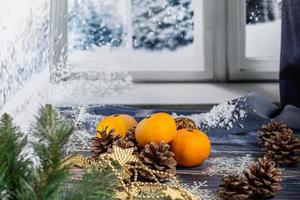 tangerinas em um fundo cinza com galhos de uma árvore de Natal, ao fundo uma janela com neve. conceito de ano novo.