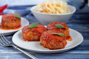 Bolinhos de peixe no suco de tomate com cebola e cenoura. dieta. Chucrute. sobre um fundo escuro de madeira. foto