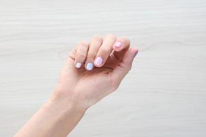 elegante manicure feminino na moda branco pastel, rosa e azul. as mãos de mulher jovem e bonita no fundo de madeira. copiar banner de espaço foto