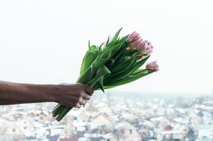 flores de tulipa na mão do homem contra um fundo desfocado urbano, vista da colina foto