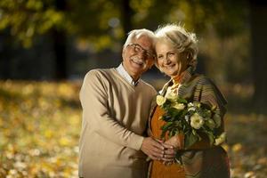 casal sênior se abraçando com um buquê de flores no parque outono foto